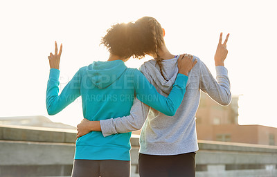 Buy stock photo Rearview shot of two female joggers doing peace signs while taking in the sunrise