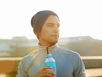 Buy stock photo Shot of a young male jogger drinking water while out for a run in the city