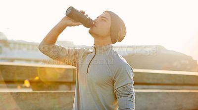 Buy stock photo Shot of a young male jogger drinking water while out for a run in the city