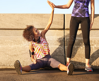 Buy stock photo Shot of a female jogger sitting on the road and high-fiving her standing partner