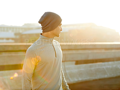Buy stock photo Shot of a young male jogger taking in the sunrise while out for a run through the city