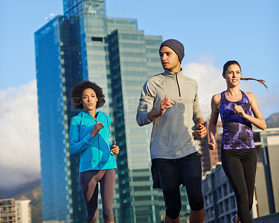 Buy stock photo Shot of three young joggers out for a run in the city streets