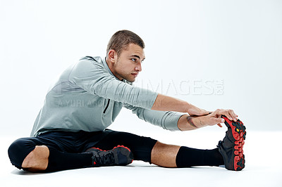 Buy stock photo Shot of a young man sitting in a studio while doing stretches