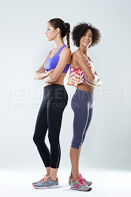 Buy stock photo Shot of two woman standing back to back in a studio wearing sports clothing