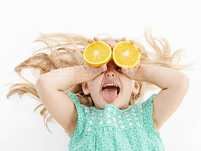 Buy stock photo Studio shot of a cute little girl playfully covering her eyes with oranges against a white background