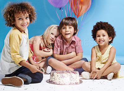 Buy stock photo Shot of a group of children sitting around a birthday cake with bunch of balloons in the background