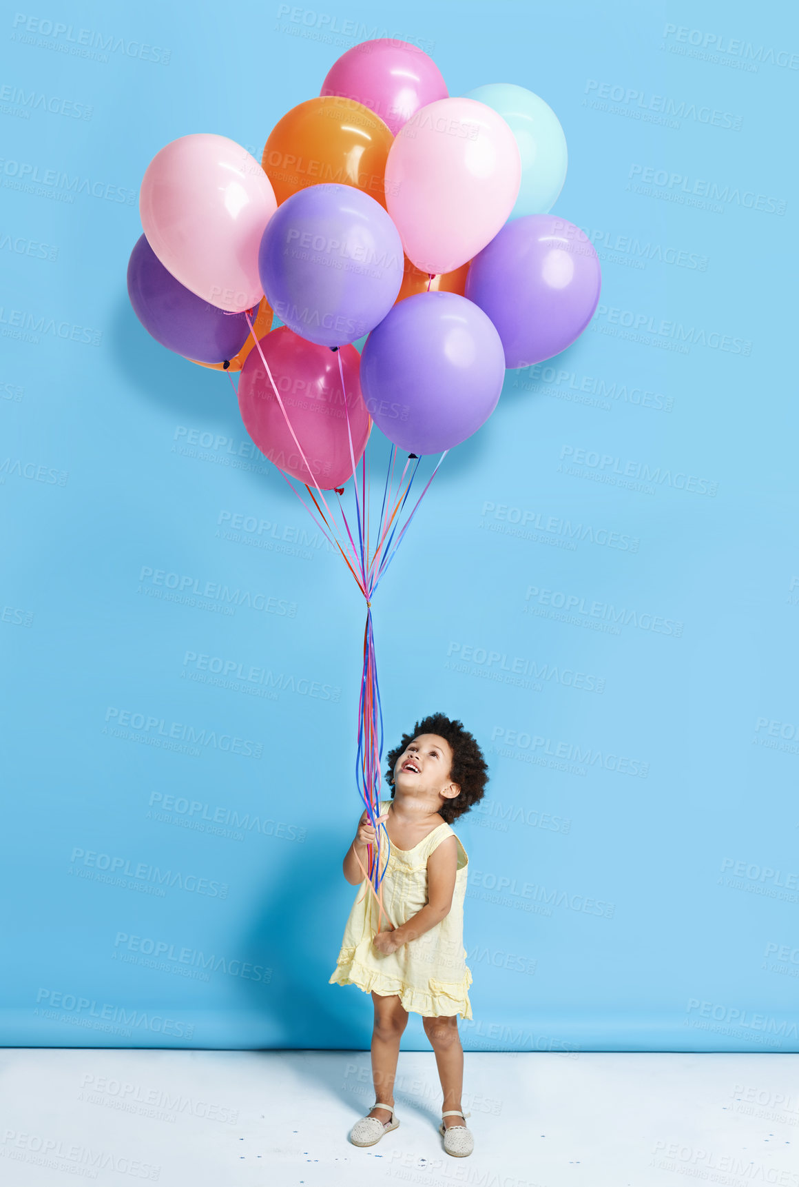 Buy stock photo Shot of a cute little girl holding a bunch of balloons against a blue background 
