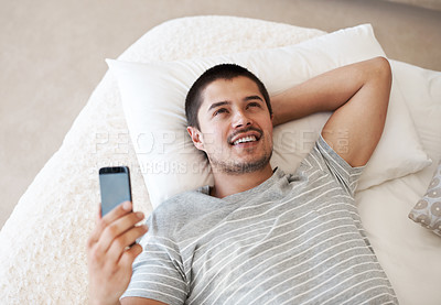 Buy stock photo Man, happy and thinking with a phone on a bed for communication, chat or notification at home. Young person relax with a smartphone and an idea for internet connection, app or social media message