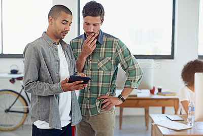 Buy stock photo Shot of two male coworkers looking at a digital tablet in an office