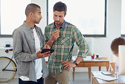 Buy stock photo Shot of two male coworkers looking at a digital tablet in an office