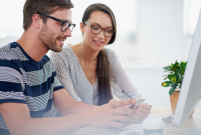 Buy stock photo Shot of two coworkers looking at a smartphone while sitting at a desk in an office