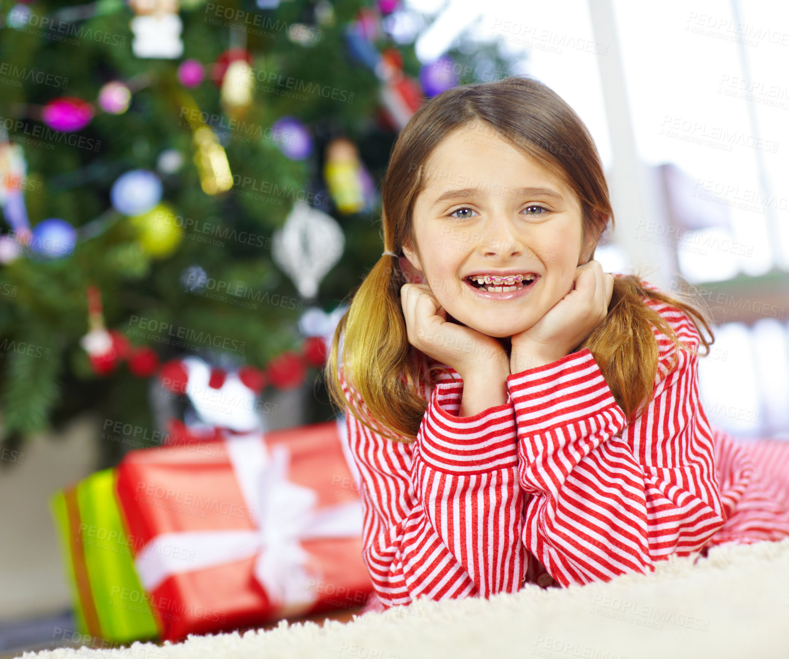 Buy stock photo An happy young girl with braces smiling at the camera with a christmas tree and presents behind her