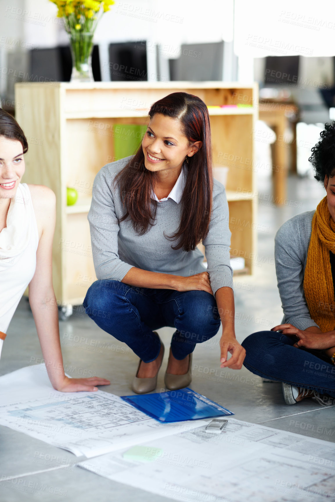 Buy stock photo A group of young employees sitting on the office floor with plans 