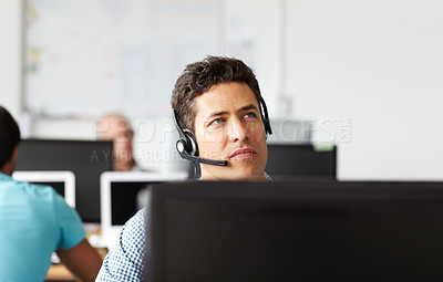 Buy stock photo A handsome young man wearing a headset looking away thoughtfully while at his desk