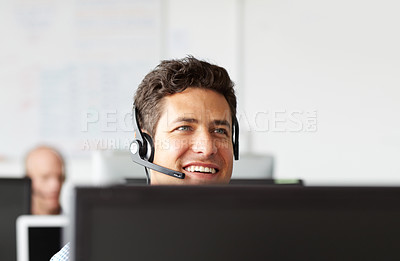Buy stock photo A young man smiling while wearing a headset and sitting at his desk