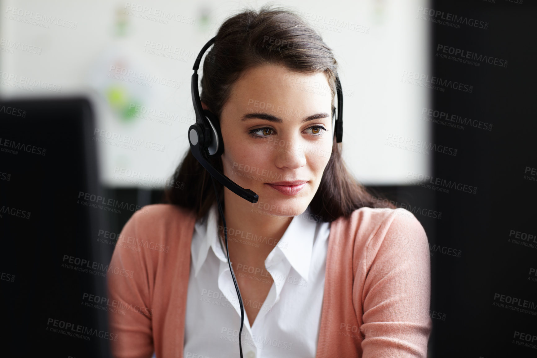 Buy stock photo A pretty young woman wearing a headset looking at her computer screen