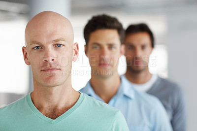Buy stock photo Shot of a young man standing in an office with male colleagues in the background