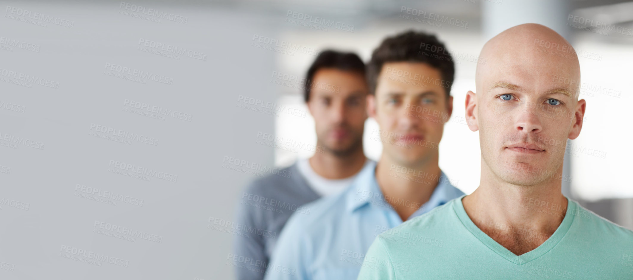 Buy stock photo Shot of a young man standing in an office with male colleagues in the background