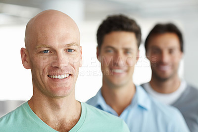 Buy stock photo Shot of a young man standing in an office with male colleagues in the background