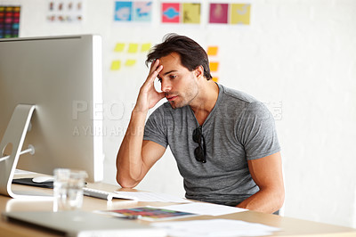 Buy stock photo A handsome man sitting at a desk and looking at a computer screen with head rested on his hand 