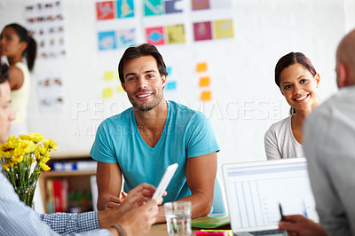 Buy stock photo Portrait of a handsome young man sitting at a table in a working a environment surrounded by colleagues