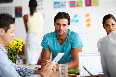 Buy stock photo Portrait of a handsome young man sitting at an office table surrounded by colleagues