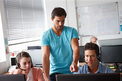 Buy stock photo A handsome man standing and pointing at a computer while two colleagues sitting on either side of hime look on