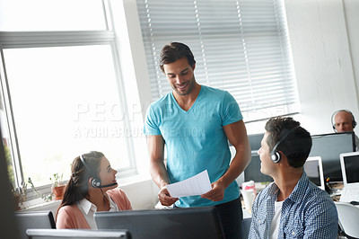 Buy stock photo A handsome man standing in an office and holding an office report while colleagues sitting at a desk look on