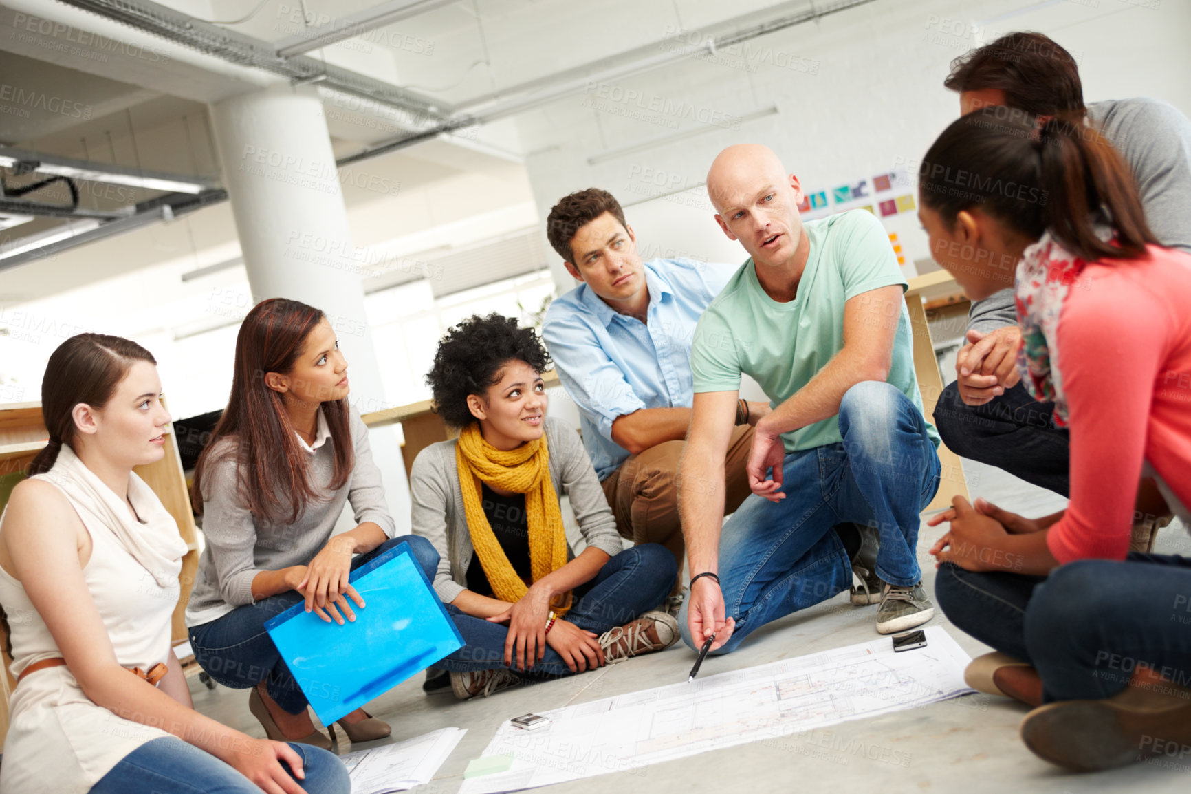 Buy stock photo A group of multi-ethnic creatives huddled together and listening to the presentation of a plan