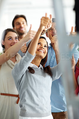 Buy stock photo A group of colleagues looking up and showing thumbs up to someone on a ladder