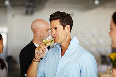 Buy stock photo A handsome young man drinking a glass of wine at an office social