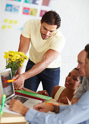 Buy stock photo A handsome young man showing his colleages something on a laptop