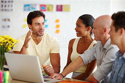 Buy stock photo A handsome young man showing his colleagues something on a laptop in front of them