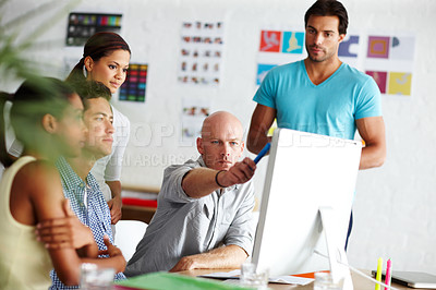 Buy stock photo A young man pointing something out to his colleagues on a computer in their office