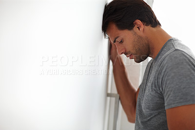 Buy stock photo Shot of a depressed-looking young man leaning his head against a wall with copyspace