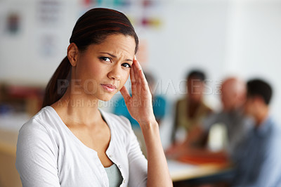 Buy stock photo Portrait of a young female professional with her hand to her temple looking in pain with coworkers in the background