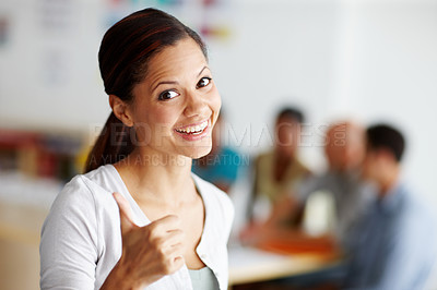 Buy stock photo Portrait of an attractive young professional smiling and giving the thumbs up while colleagues work in the background