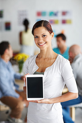 Buy stock photo Portrait of a young professional showing a digital tablet screen with her coworkers sitting in the background
