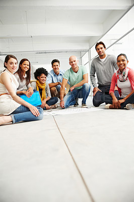 Buy stock photo Shot of a large group of positive-looking young designers kneeling on the floor looking at blueprints