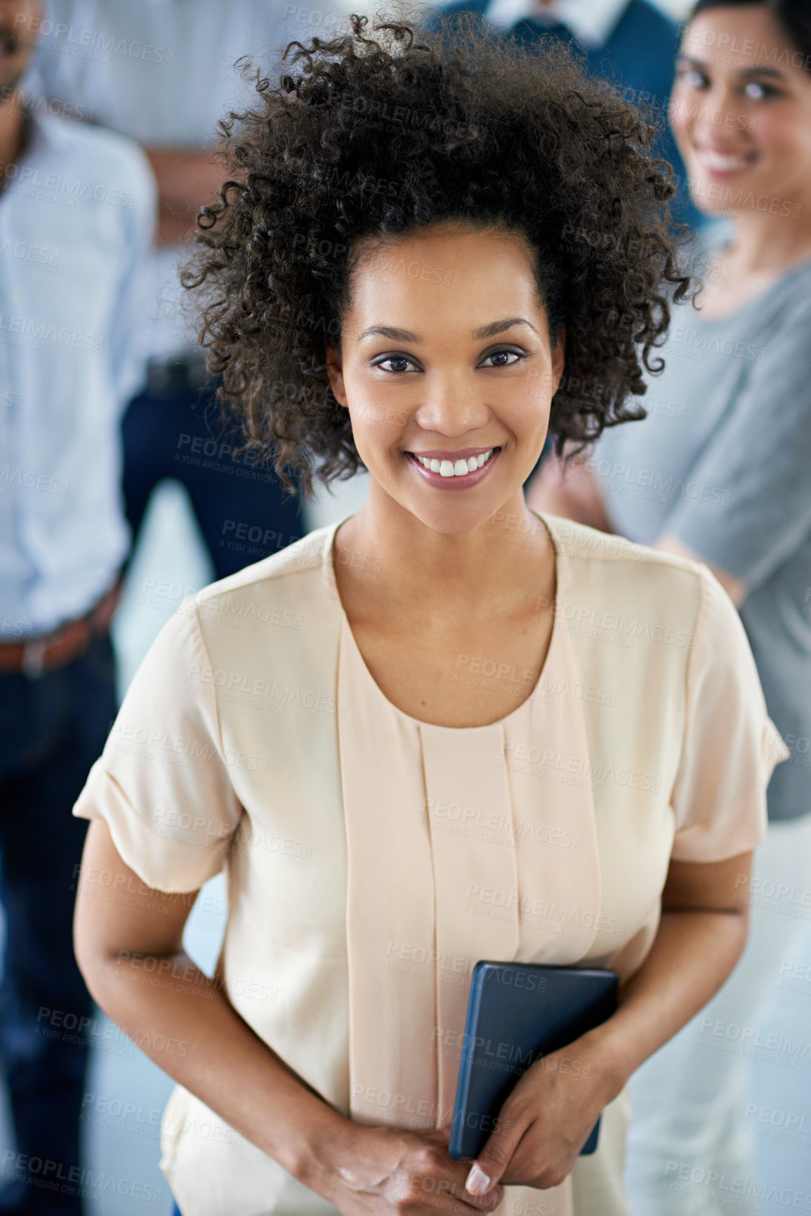 Buy stock photo Portrait of a smiling young office worker standing in an office with colleagues in the background