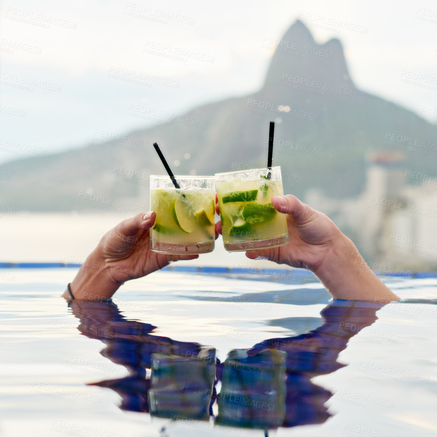 Buy stock photo Cropped shot of two people toasting in a pool with a view