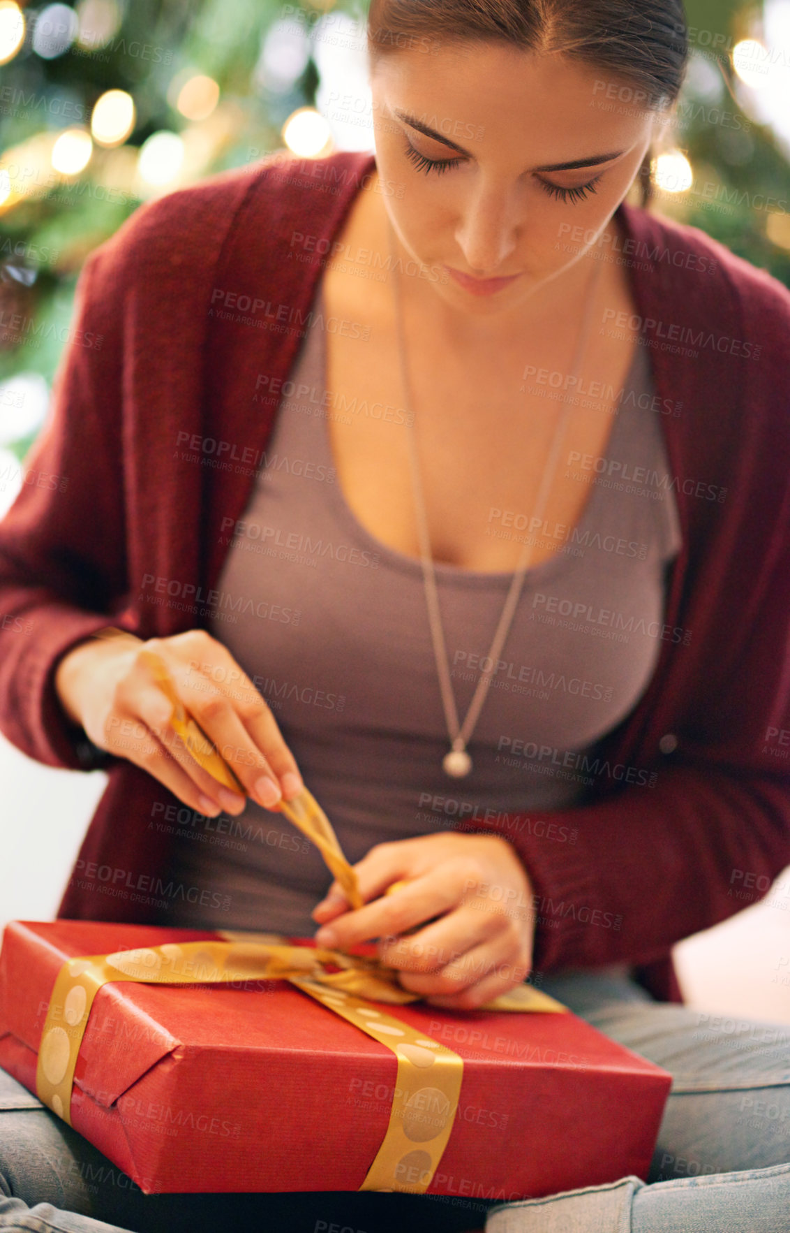 Buy stock photo Shot of a beautiful young woman opening a present in front of a christmas tree