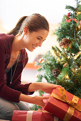 Buy stock photo Shot of an attractive young woman looking through presents under a christmas tree