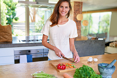 Buy stock photo Shot of an attractive young woman chopping vegetables in a kitchen
