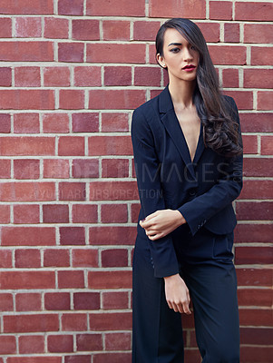 Buy stock photo Shot of a beautiful woman wearing a classic feminine suit leaning against a brick wall