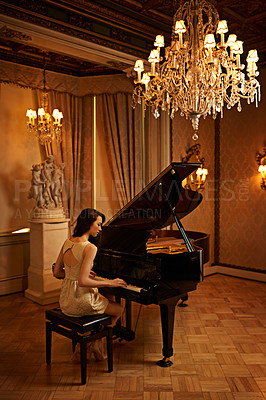 Buy stock photo Shot of a beautiful young woman playing the piano in an elegant room