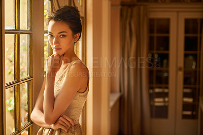Buy stock photo Portrait of a beautiful and elegant young woman standing by a window