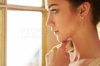 Buy stock photo Shot of a beautiful young woman looking through a window