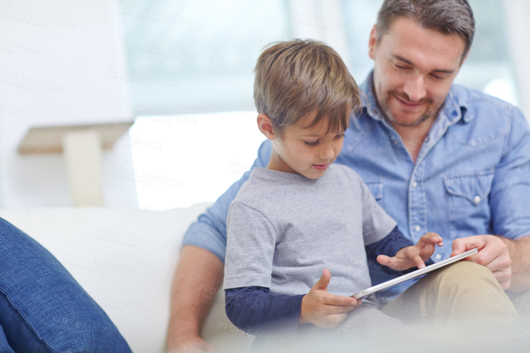 Buy stock photo Shot of an adorable little boy using a digital tablet with his father at home