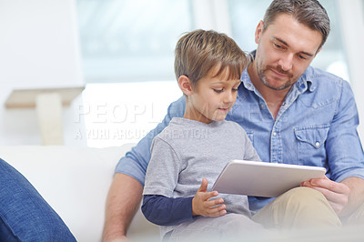 Buy stock photo Shot of an adorable little boy using a digital tablet with his father at home